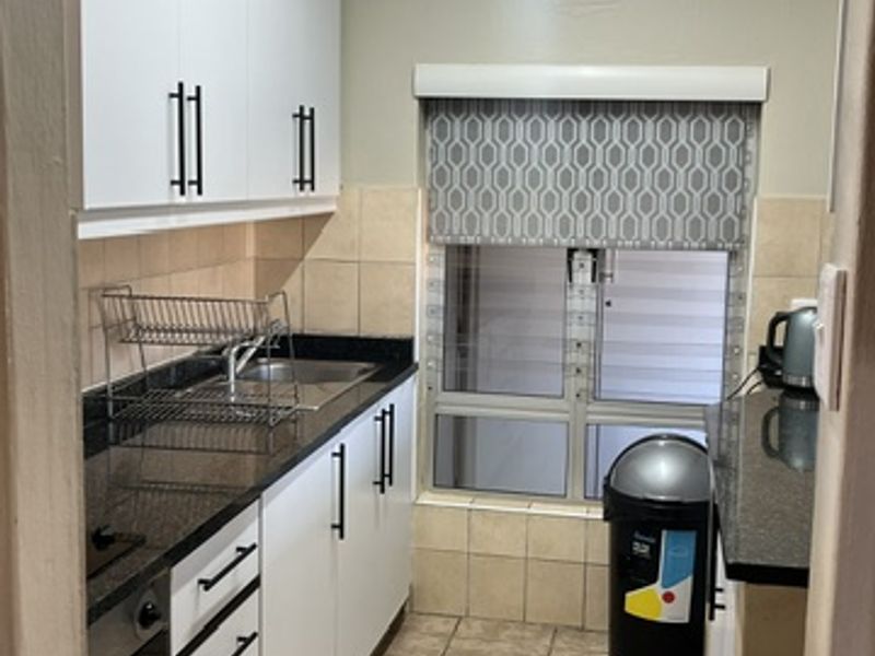 A functional galley-style kitchen featuring white cabinetry, dark granite countertops, built-in oven, and tiled flooring with a window for natural light.
