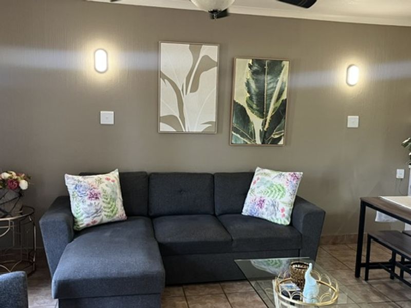A comfortable living room featuring tiled flooring, wall-mounted lighting, a ceiling fan, and built-in shelving, creating a functional and inviting space.