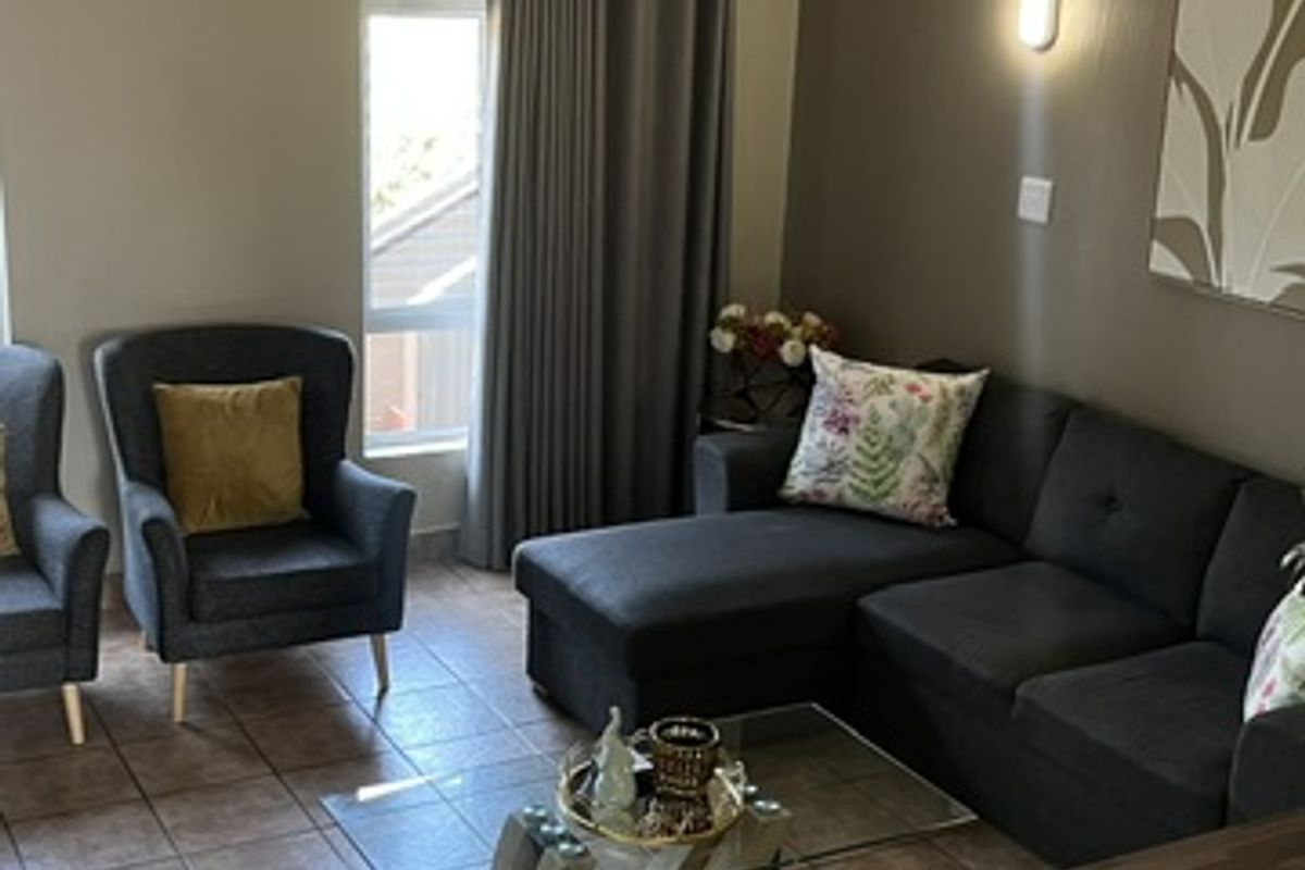 A comfortable living room featuring tiled flooring, a ceiling fan, and wall-mounted lighting, providing a functional and inviting space.