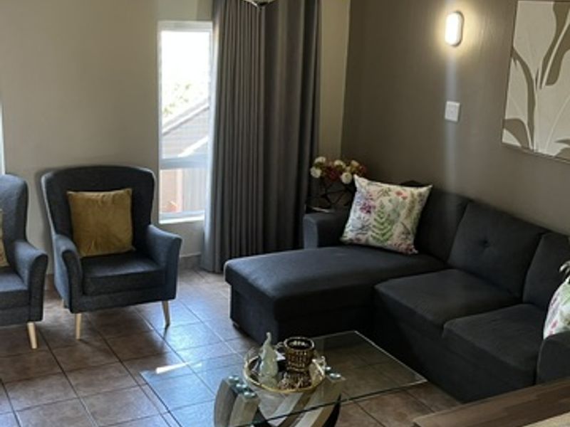 A comfortable living room featuring tiled flooring, a ceiling fan, and wall-mounted lighting, providing a functional and inviting space.