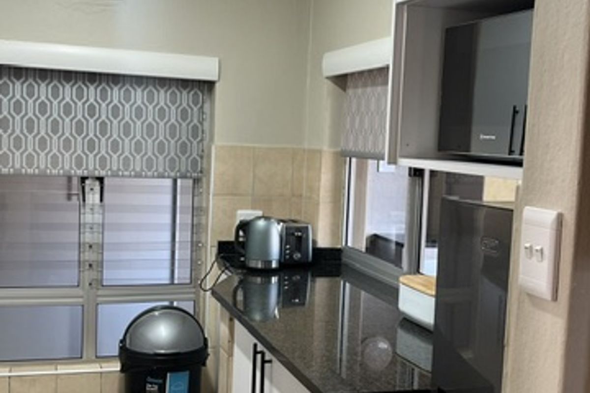 A compact kitchen featuring granite countertops, tiled flooring, built-in cabinetry, and a built-in microwave, offering a functional layout for an apartment.