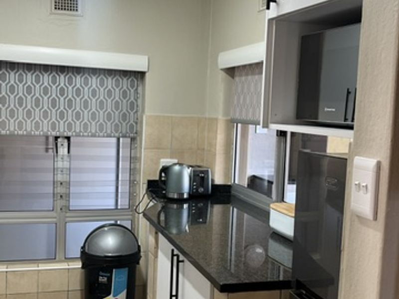 A compact kitchen featuring granite countertops, tiled flooring, built-in cabinetry, and a built-in microwave, offering a functional layout for an apartment.