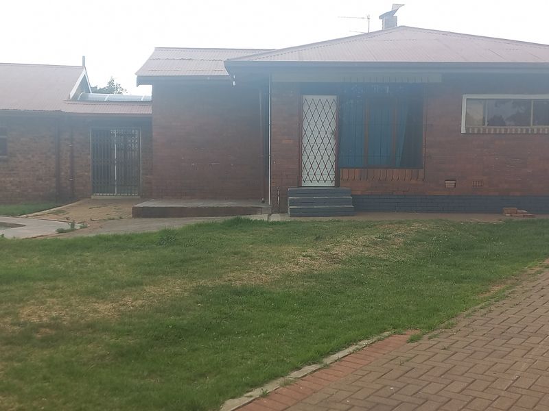 Rear view of a single-story brick house featuring a swimming pool, paved driveway, and security features on doors and windows.