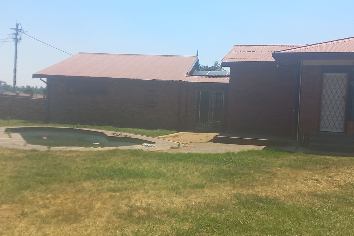 Rear view of the property featuring a brick exterior, metal roof, and an outdoor swimming pool set within a large garden area.
