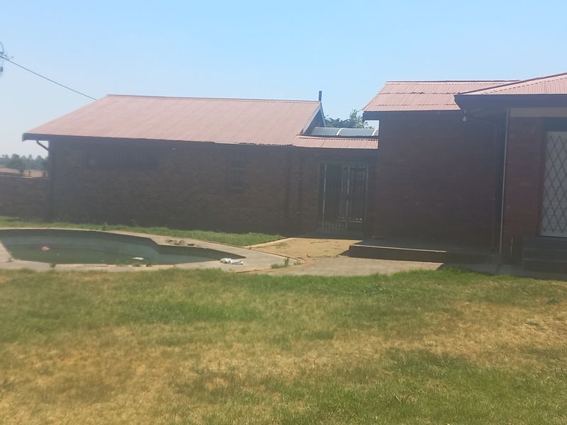Rear view of the property featuring a brick exterior, metal roof, and an outdoor swimming pool set within a large garden area.