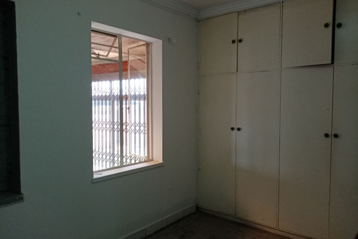 An empty bedroom featuring built-in cupboards, a window with a security gate, and crown molding, offering a blank canvas for renovation.
