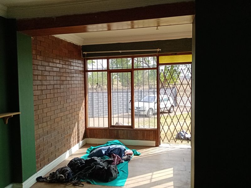 A living area featuring exposed brick walls, timber-framed windows with security bars, and direct access to the exterior through a security gate.