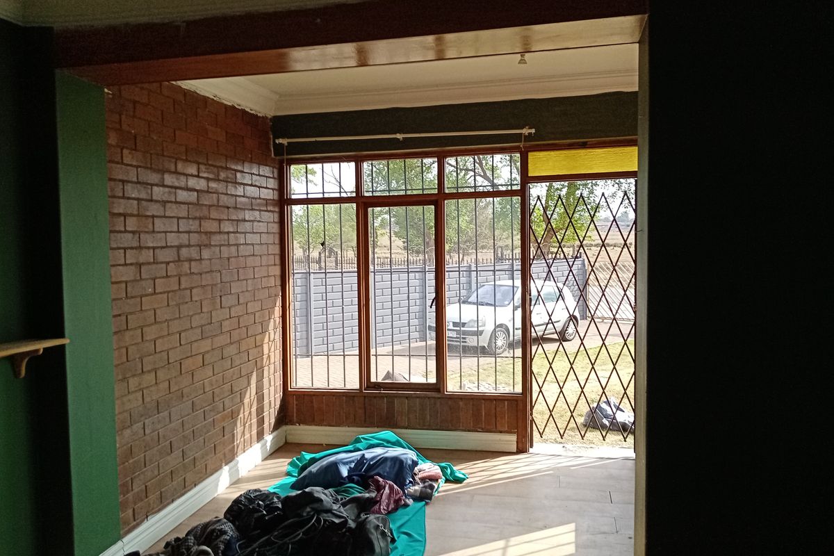 A living area featuring exposed brick walls, timber-framed windows with security bars, and direct access to the exterior through a security gate.