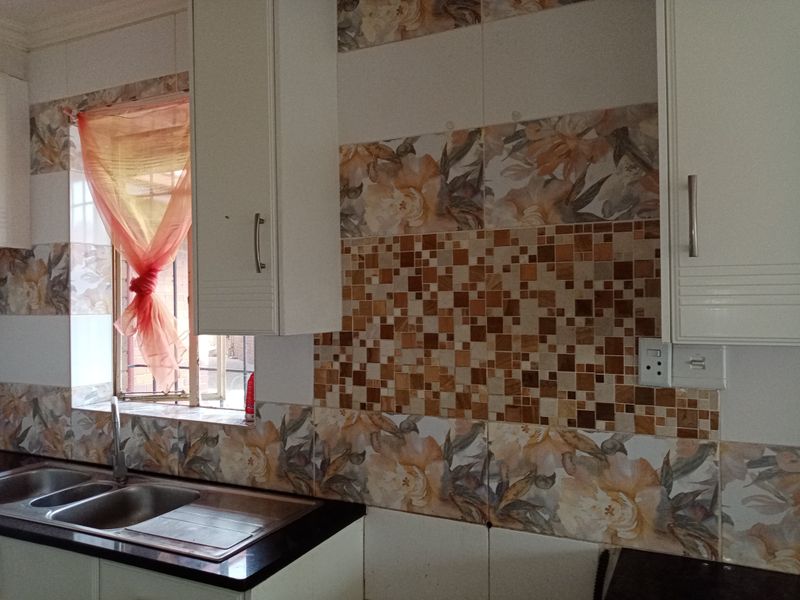 A kitchen area featuring white built-in cabinetry, a double bowl stainless steel sink, and decorative floral and mosaic tiled backsplash.