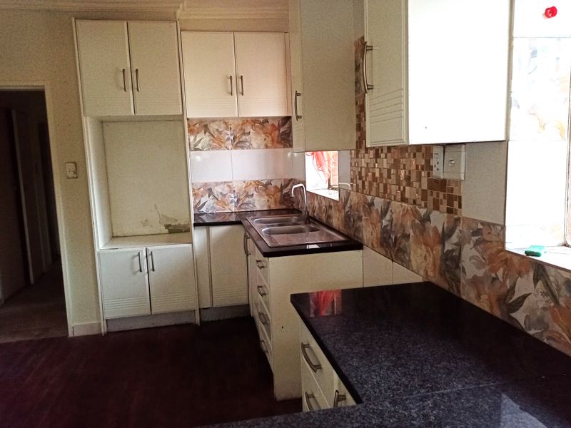 A dated kitchen featuring built-in cabinetry, laminate countertops, and a double bowl sink with tiled backsplash, requiring cosmetic updates.