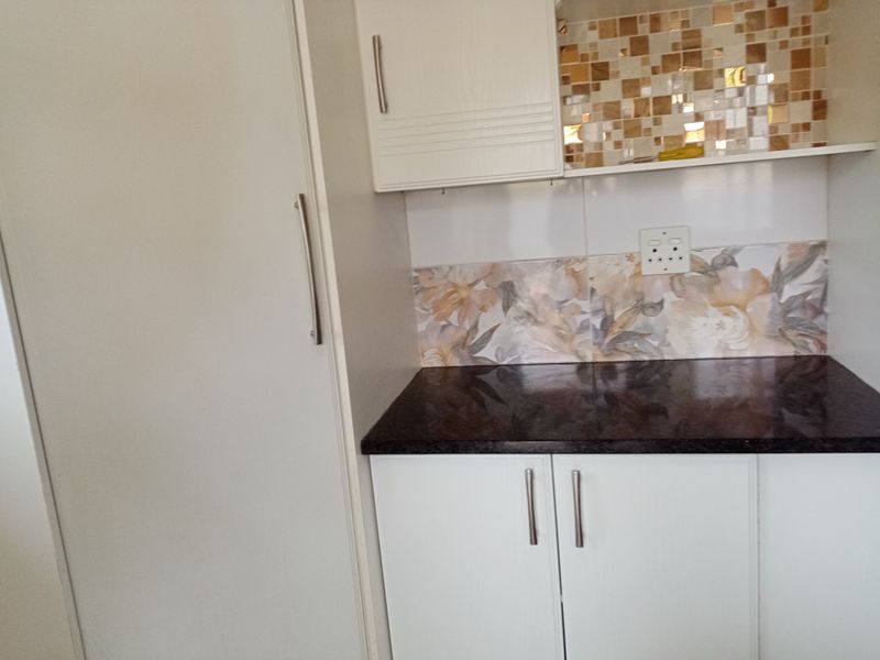 A clean kitchen corner featuring white built-in cabinetry, dark granite countertops, and a decorative mosaic and floral tile backsplash.