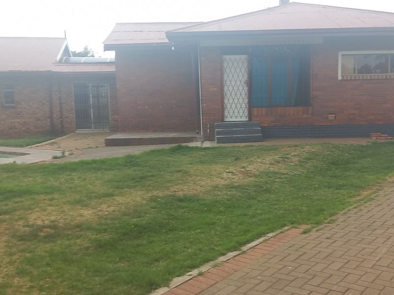 Rear view of a brick house featuring a swimming pool, paved driveway, and security features on doors and windows.