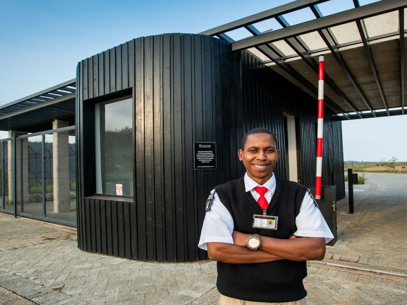 Modern security entrance gatehouse featuring dark timber cladding, a paved driveway, and a functional boom gate system for controlled property access.