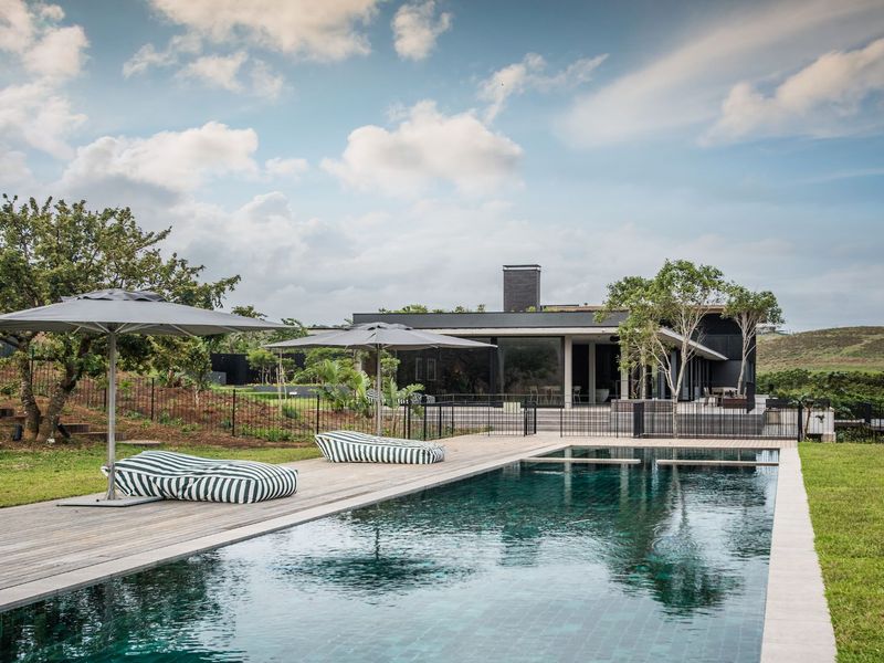 A modern outdoor pool area featuring a rectangular swimming pool, timber decking, and a landscaped garden with views of the surrounding landscape.