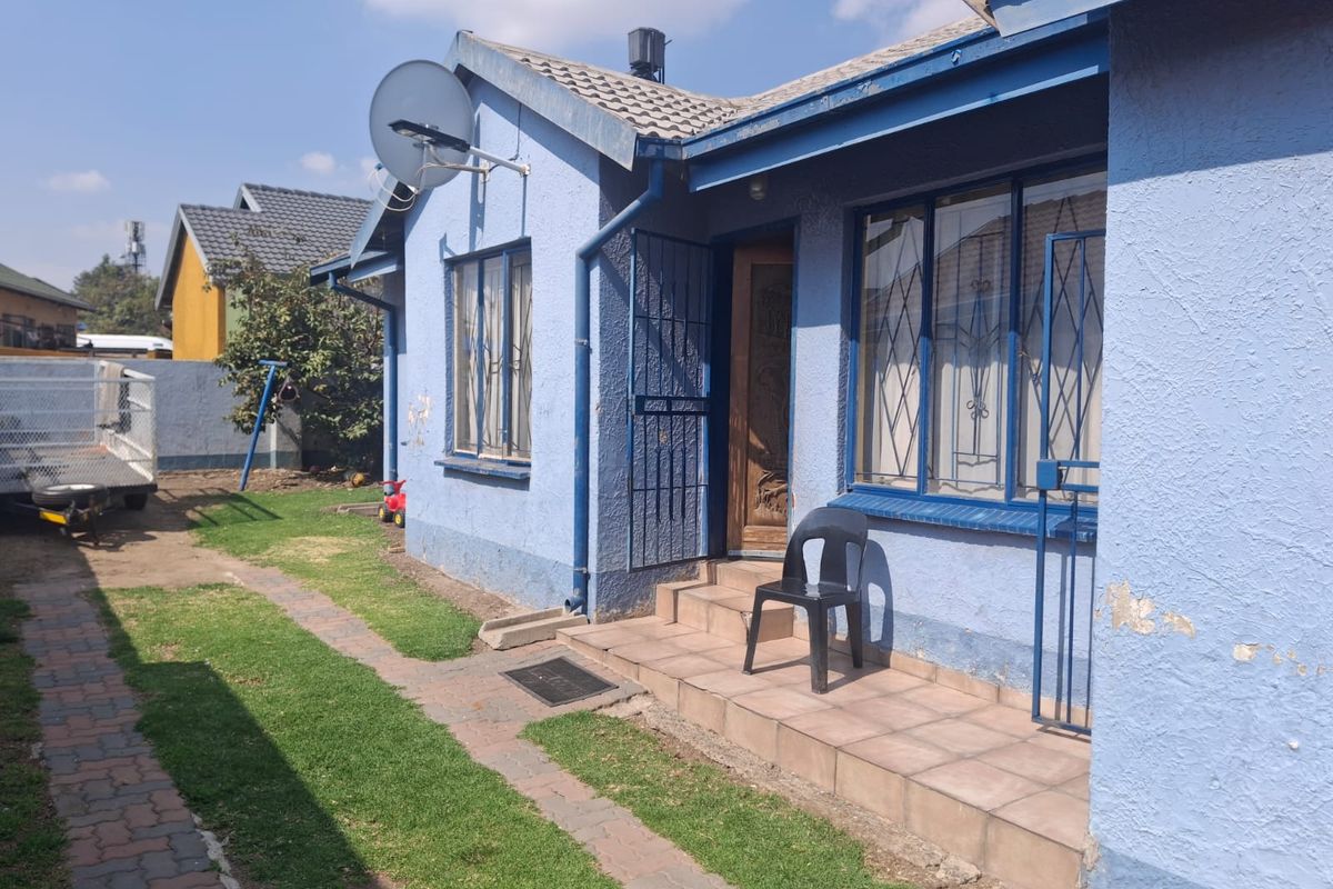 Rear exterior view of the house featuring a tiled porch, security gates, and a paved walkway leading to the garden area.