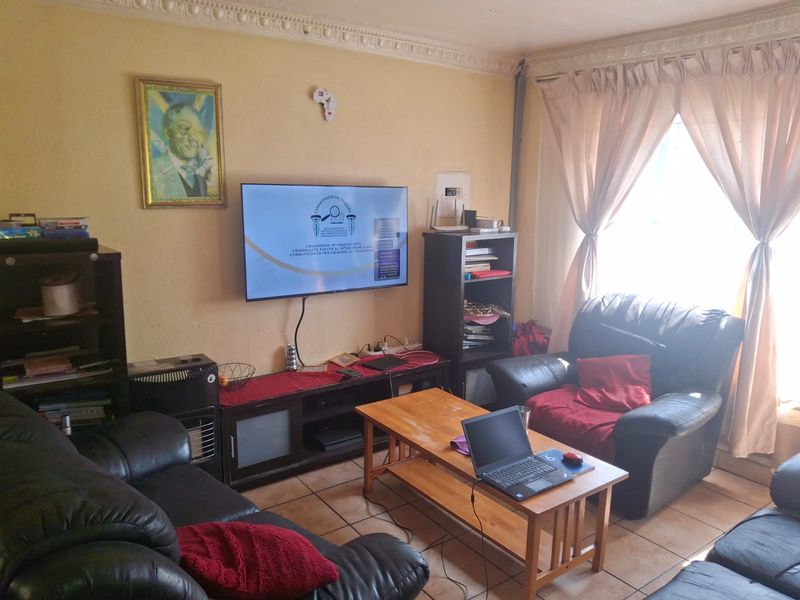 A living room featuring tiled flooring and decorative ceiling cornicing, currently used as a lounge area.