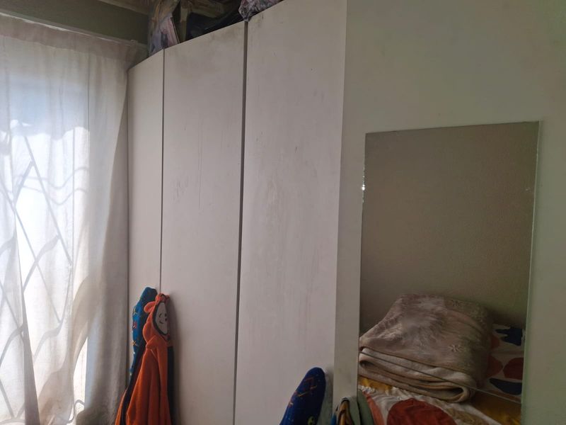 A bedroom featuring a built-in wardrobe with visible surface wear and a wall-mounted mirror.