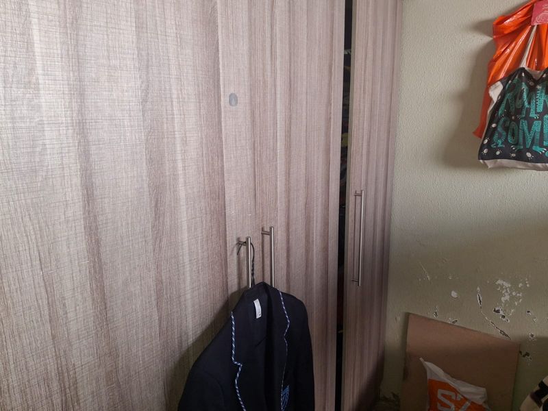 Bedroom featuring a wood-grain finish built-in wardrobe with metal handles, showing signs of wall surface wear.