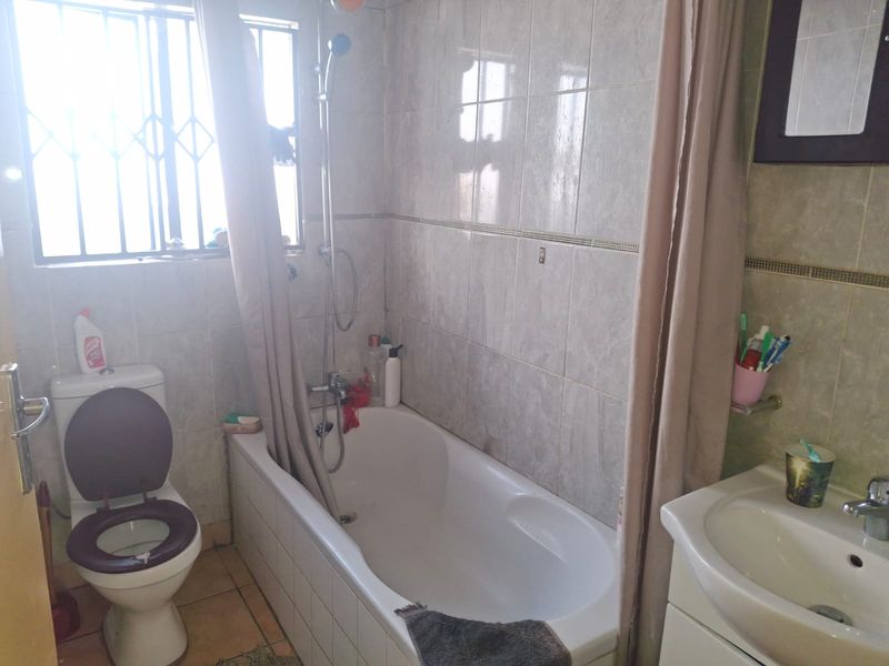 A functional bathroom featuring a bathtub with shower attachment, a vanity basin, and tiled walls, equipped with security bars on the window.