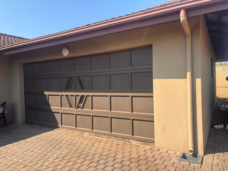 A well-maintained single garage featuring a decorative sectional door, paved driveway, and functional exterior drainage system.
