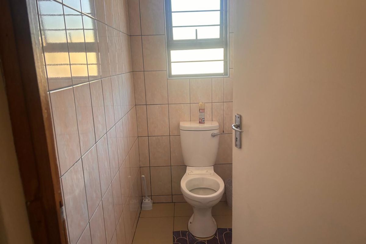 A compact bathroom featuring full-height ceramic wall tiling, tiled flooring, and a standard toilet suite with a window for natural light.