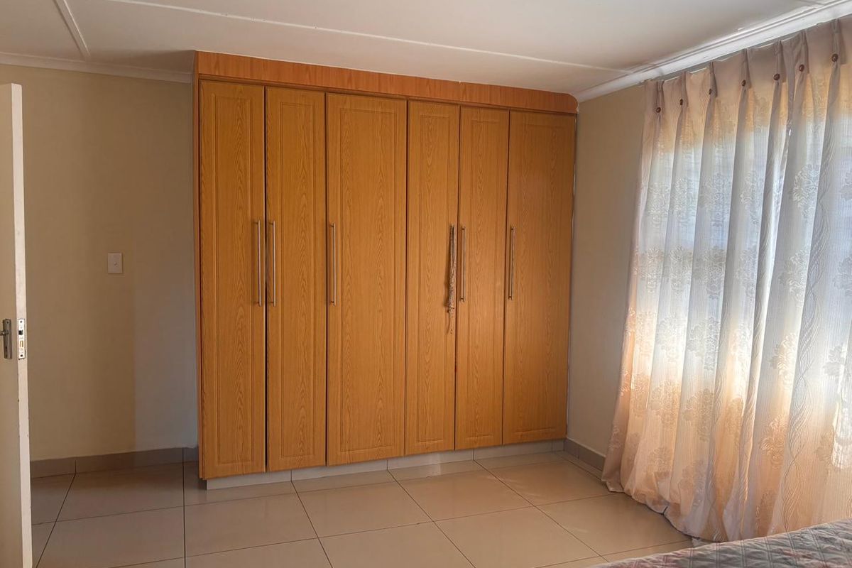 A bedroom featuring light-toned tiled flooring and extensive built-in wooden cupboards providing ample storage space.