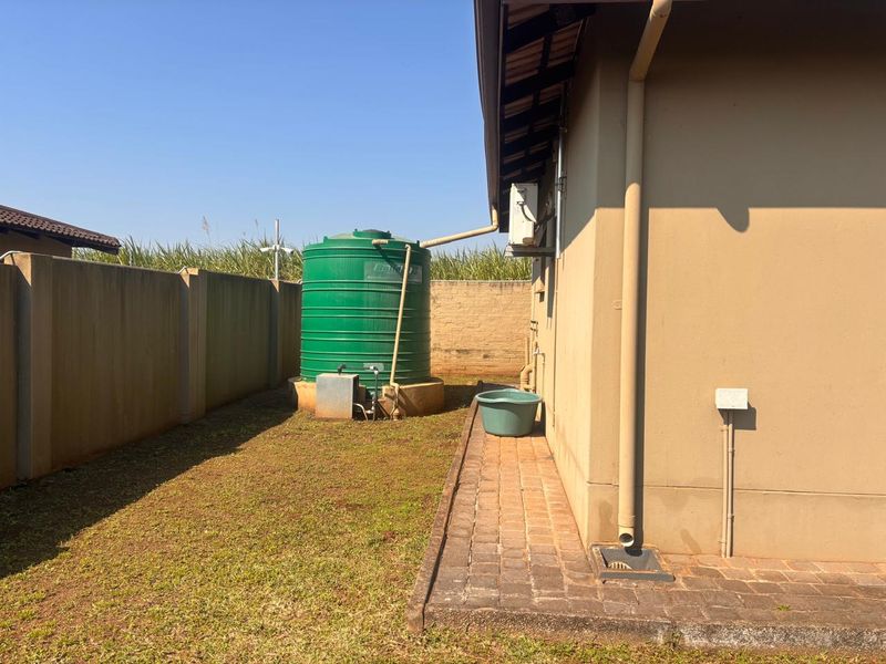 Rear exterior view of the townhouse featuring a water storage tank, paved walkway, and boundary wall.