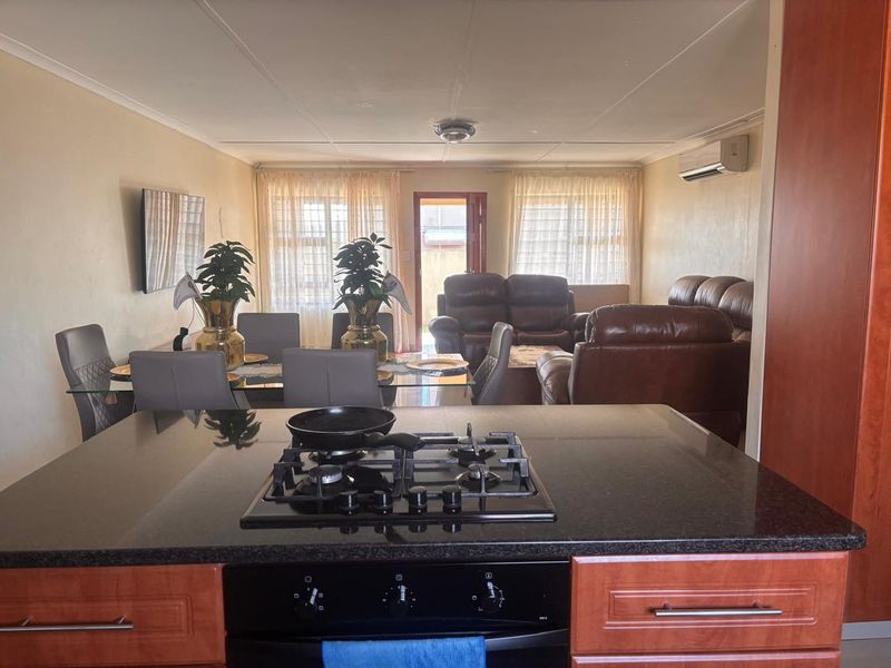 Open-plan living and dining area featuring a kitchen island with a gas hob, built-in oven, and granite countertops, flowing into the main living space.