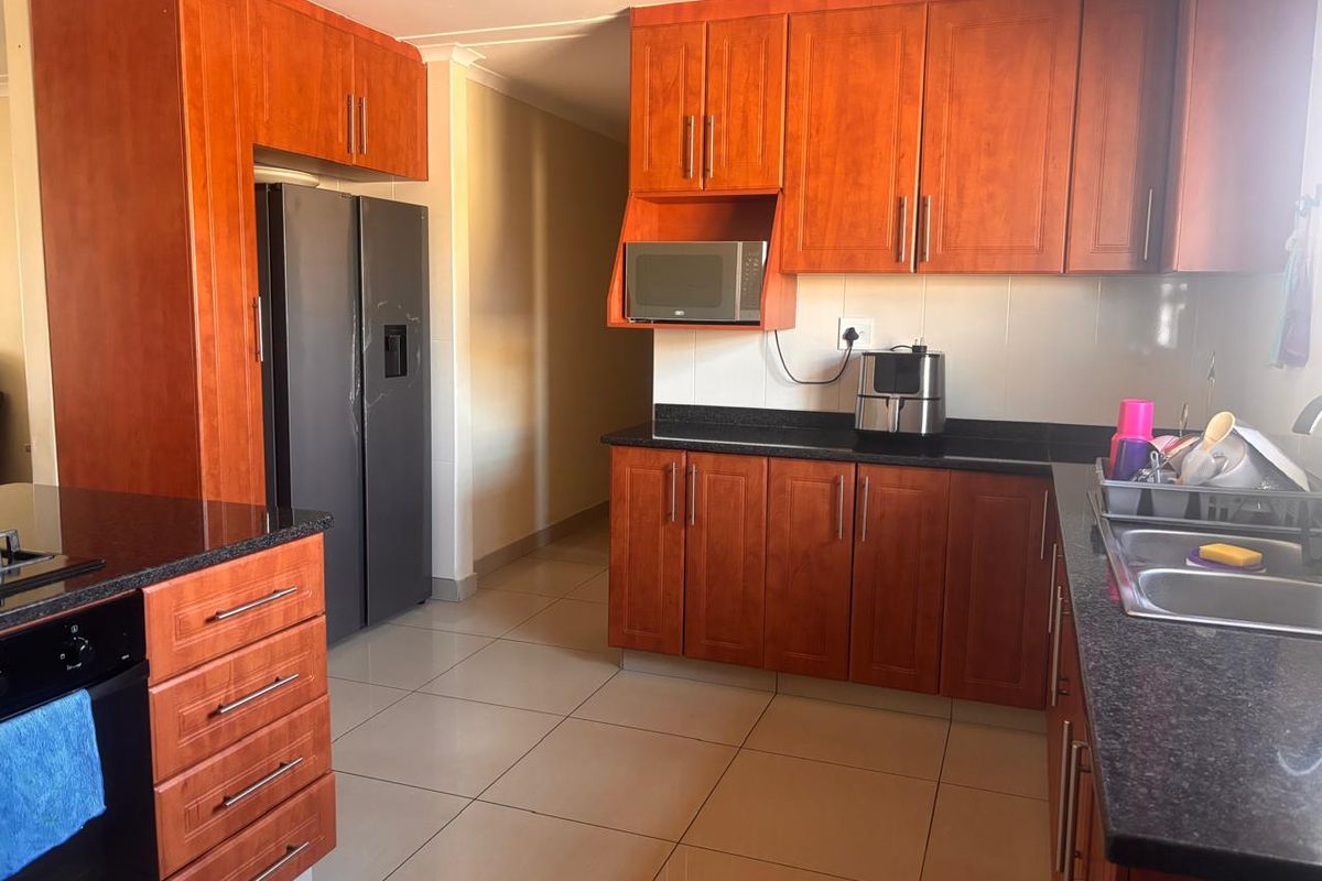 A functional kitchen featuring warm-toned wooden cabinetry, dark granite countertops, tiled flooring, and integrated appliances including an oven and microwave.