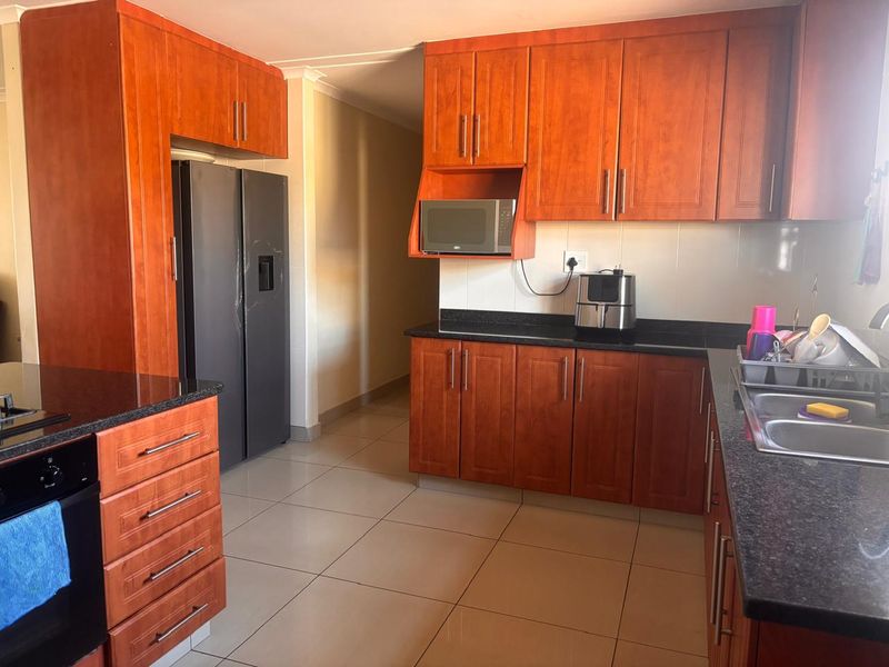 A functional kitchen featuring warm-toned wooden cabinetry, dark granite countertops, tiled flooring, and integrated appliances including an oven and microwave.