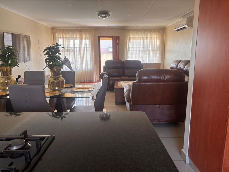 Open-plan living and dining area featuring tiled floors, a split-system air conditioner, and a kitchen with a granite countertop and gas hob.