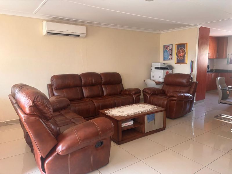 Open-plan living area featuring tiled flooring, a wall-mounted air conditioning unit, and an adjacent kitchen with built-in cabinetry.