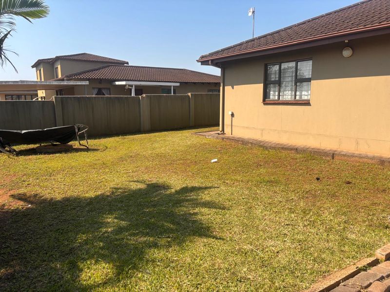 A private rear garden area featuring a lawn, perimeter walling, and a view of the townhouse exterior with a tiled roof.