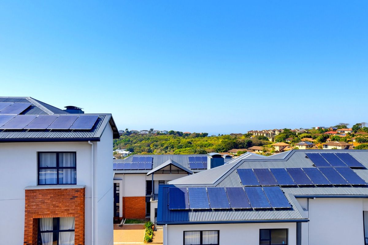 An elevated aerial view of modern apartment buildings featuring metal roofs with integrated solar panel arrays and a mix of brick and rendered facades.