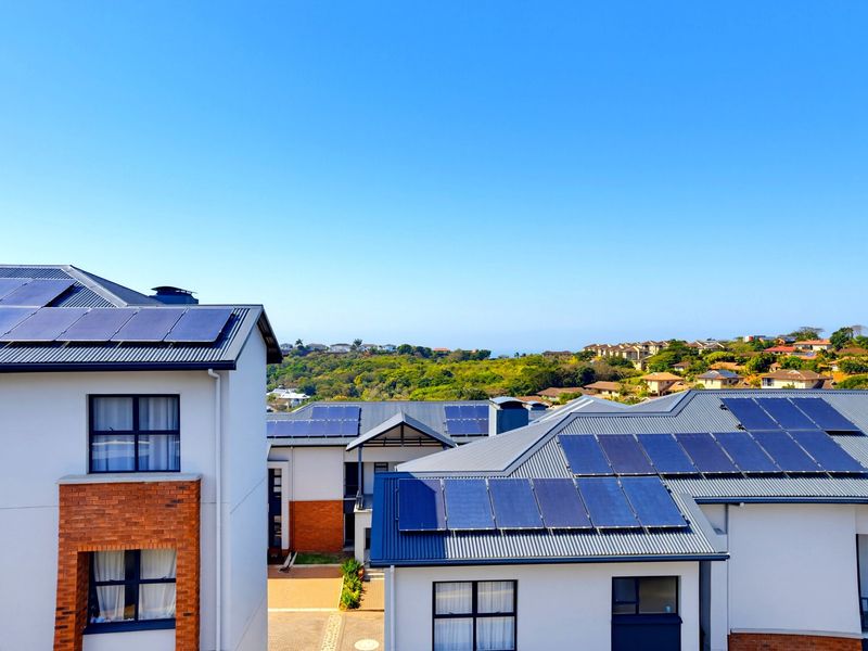 An elevated aerial view of modern apartment buildings featuring metal roofs with integrated solar panel arrays and a mix of brick and rendered facades.