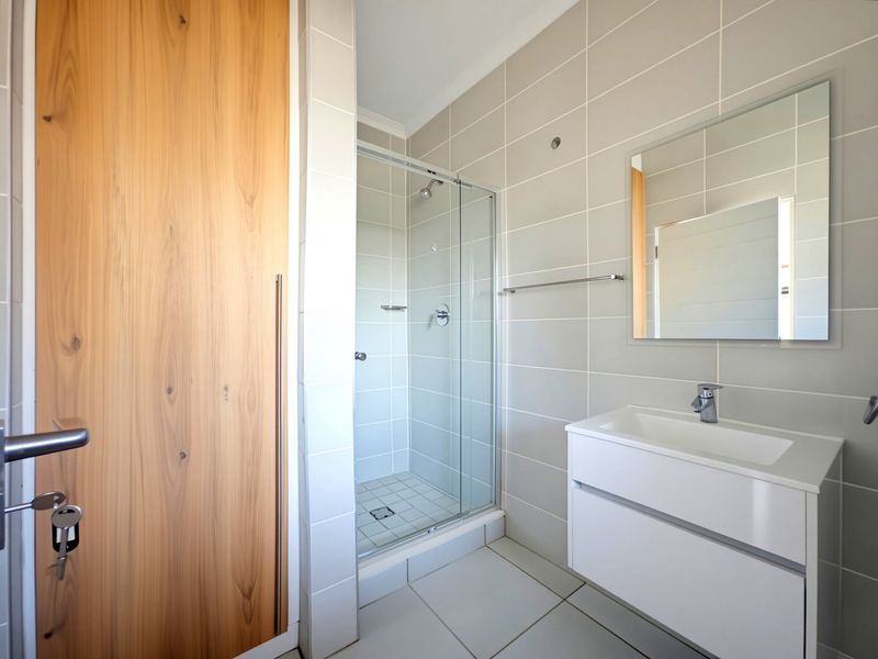 Modern bathroom featuring a glass shower enclosure, wall-mounted vanity with basin, and neutral tiled finishes throughout.