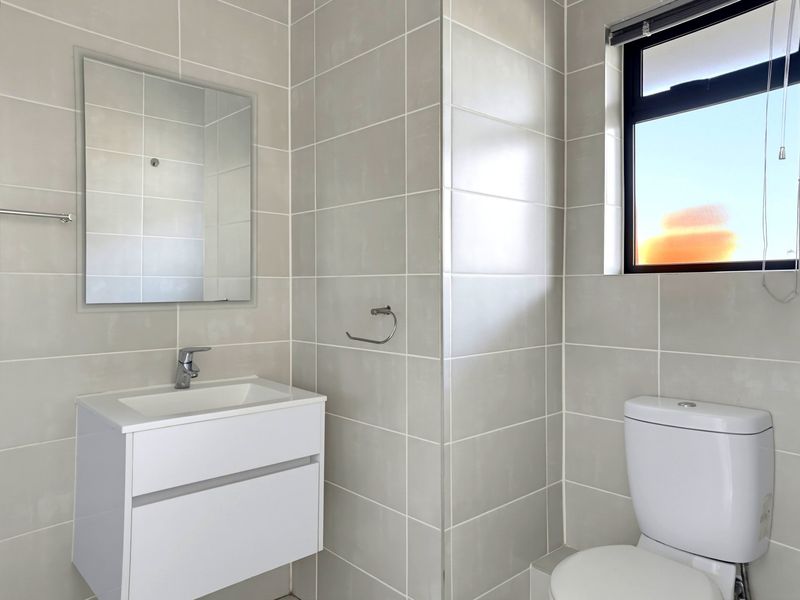 A clean, modern bathroom featuring neutral wall tiles, a wall-mounted vanity with basin, and a toilet.