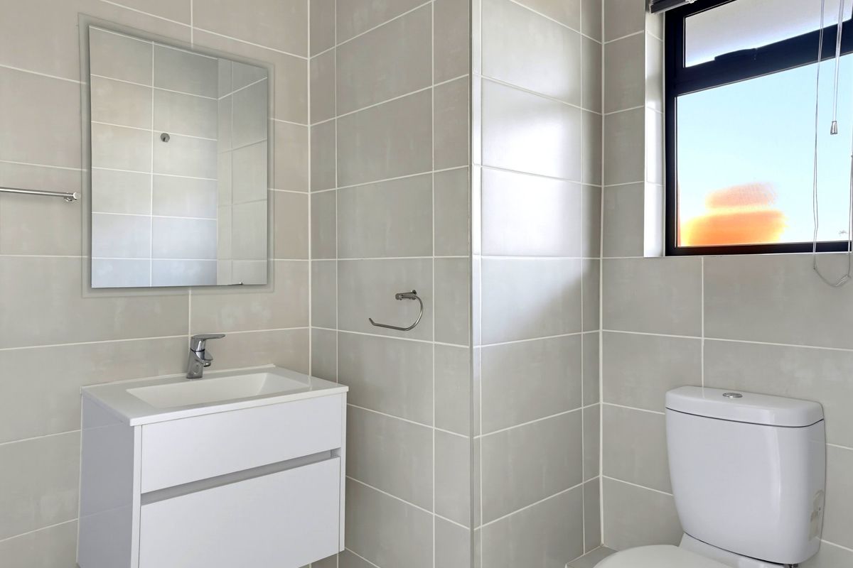 A clean, modern bathroom featuring neutral wall tiles, a wall-mounted vanity with basin, and a toilet.