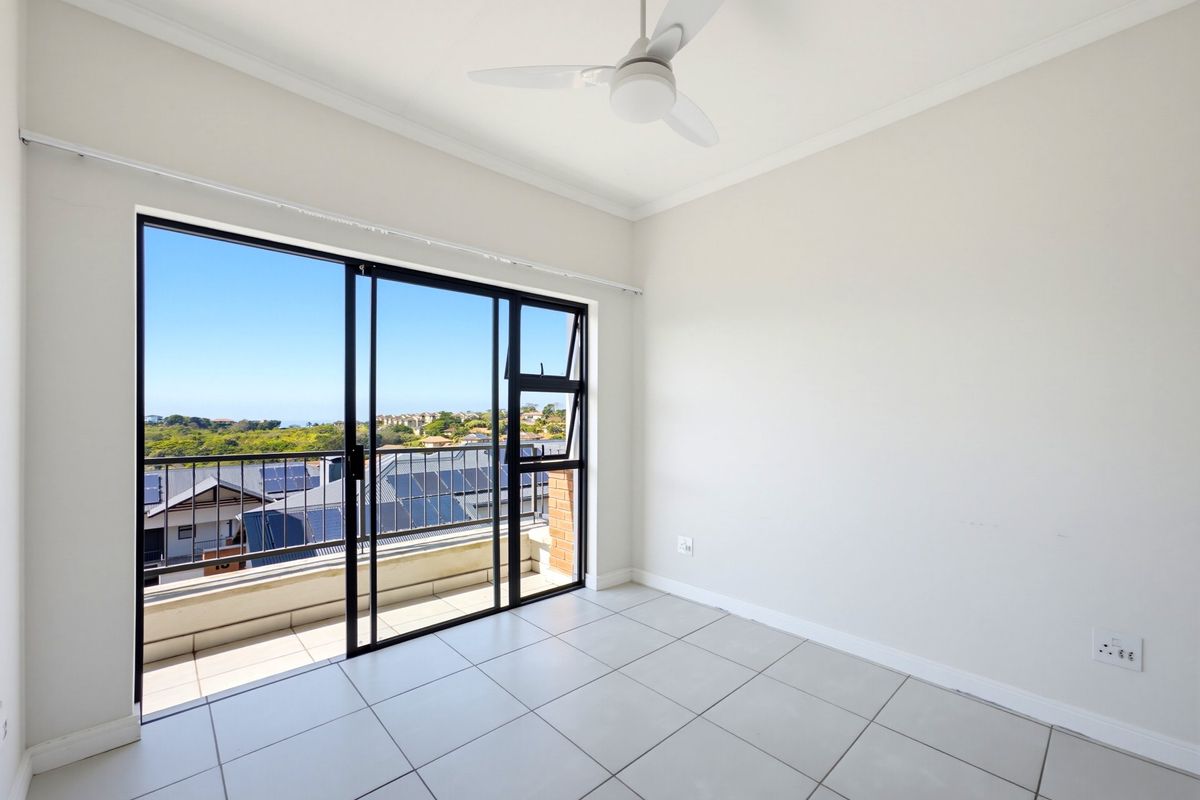 A bright, empty bedroom featuring tiled flooring, a ceiling fan, and large sliding glass doors opening onto a balcony with scenic views.