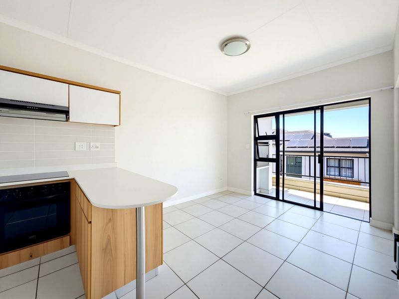 Bright open-plan kitchen and living area featuring modern cabinetry, built-in appliances, tiled flooring, and direct access to a private balcony.