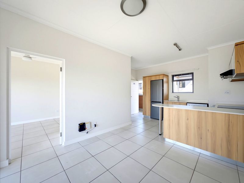 Bright open-plan living and kitchen area featuring modern wood-look cabinetry, tiled flooring, and a functional kitchen island with integrated fixtures.