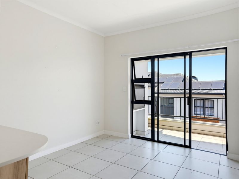 Bright and spacious open-plan living area featuring neutral tiled flooring and a large black aluminium sliding door leading to a private balcony.