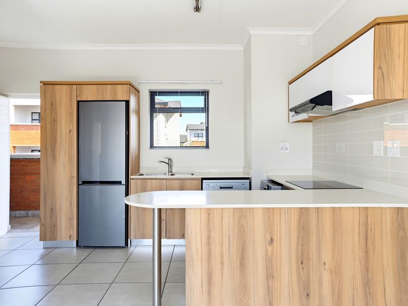 Modern kitchen featuring wood-grain cabinetry, stone countertops, integrated hob, extractor fan, and a breakfast bar, complemented by neutral tiled flooring.