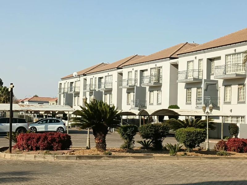 Exterior view of a multi-story apartment complex featuring tiled roofs, private balconies, covered parking bays, and well-maintained landscaped garden areas.