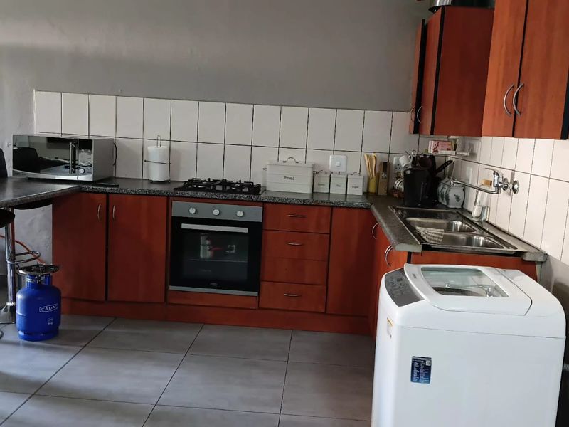 A functional kitchen featuring wooden cabinetry, granite countertops, a gas hob, built-in oven, and tiled backsplash with integrated sink and laundry plumbing.