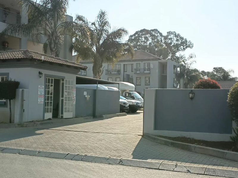 View of the apartment complex entrance featuring a security gatehouse, paved driveway, and perimeter walling.
