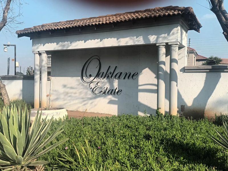 The entrance signage and perimeter wall of Oaklane Estate, featuring a tiled roof structure and integrated security fencing.