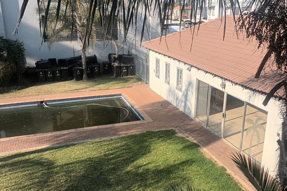 Rear exterior view of the property featuring a swimming pool, paved patio area, and lawn, with sliding glass doors leading into the building.
