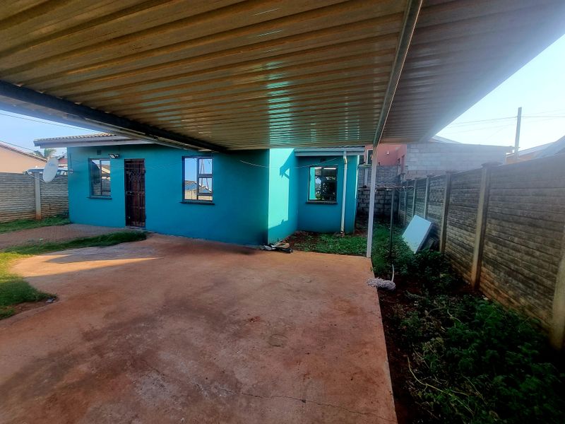 Rear exterior view featuring a large corrugated metal carport, concrete driveway, and secure boundary walling surrounding the property.