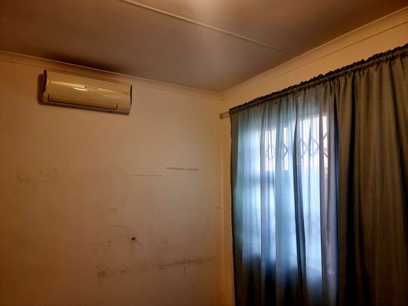An empty bedroom featuring a wall-mounted air conditioning unit and a window fitted with a security gate.